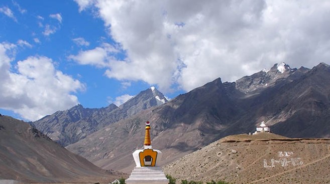A white and gold stupa in a broad Himalayan valley, with the letters LMHS marked out in stone on the hillside behind it.