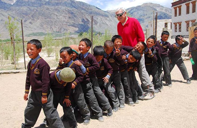A long line of Lamdon students in maroon uniforms laughing on a dusty school ground, with bare Zanskar mountains behind.