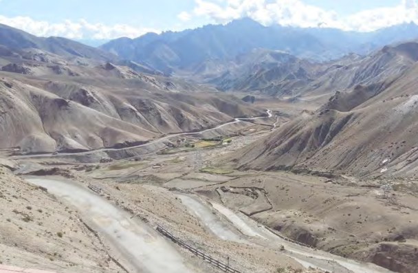 A winding mountain road cut into arid ridges above a river in the Zanskar valley.